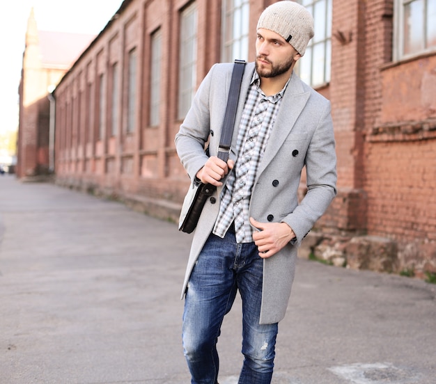 Premium Photo | City life. stylish young man in grey coat and hat walking  on the street in the city.