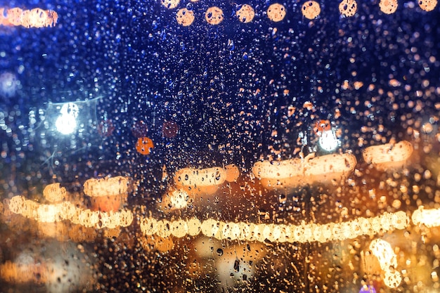 City lights of the night during the rain behind a glass covered with drops of water.