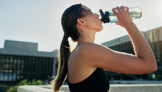 City profile or woman drinking water on break in exercise running workout or fitness training Girl athlete relax or thirsty sports runner with liquid bottle for wellness or hydration in England