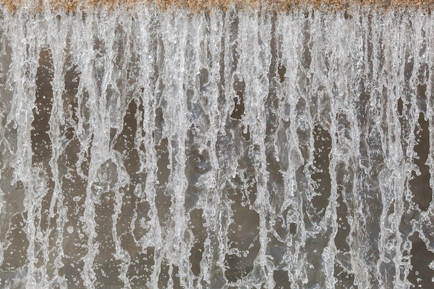 City river waterfall large cascade wall close-up on a summer day, side view of the falling water flow and water foam at the bottom