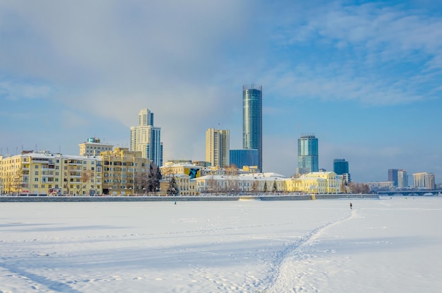 A city skyline is seen behind a frozen river.