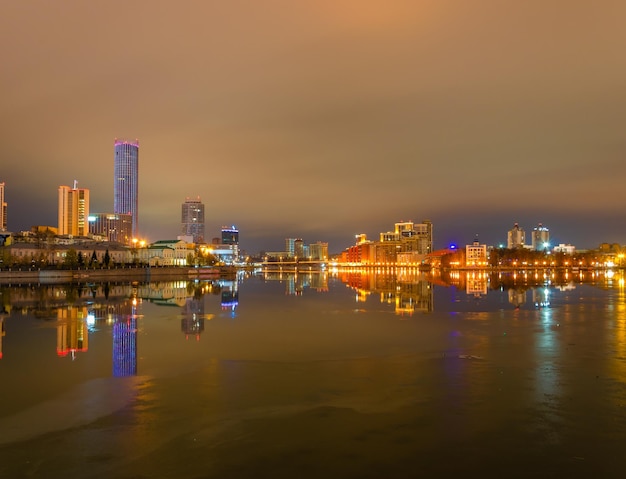 A city skyline with lights on the buildings and a body of water