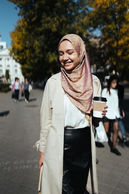 On the city street laughing muslim woman drinking coffee and looking down