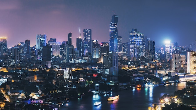 Cityscape of Bangkok city skyline at night with light streaks of boat in Thailand,