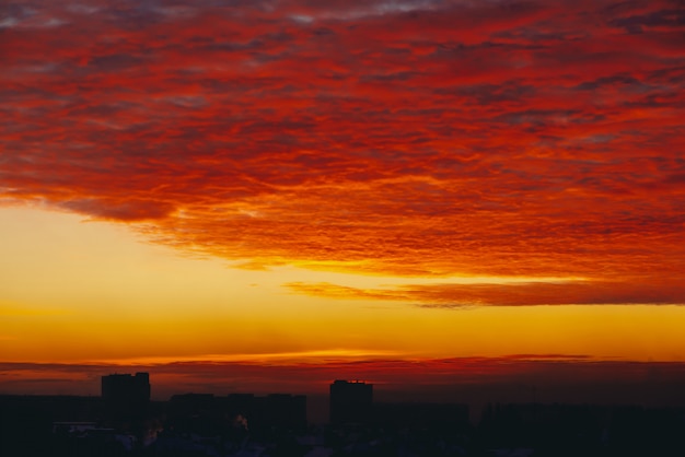 Cityscape met vurige bloed vampire dageraad. Verbazingwekkende warme dramatische bewolkte hemel boven donkere silhouetten van stadsgebouwen. Oranje zonlicht. Atmosferische achtergrond van zonsopgang bij bewolkt weer. Kopieer ruimte.