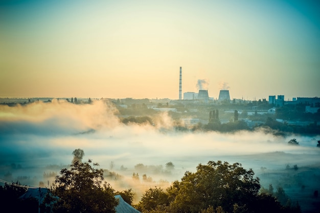 Paesaggio urbano di centrali elettriche e campo con nebbia