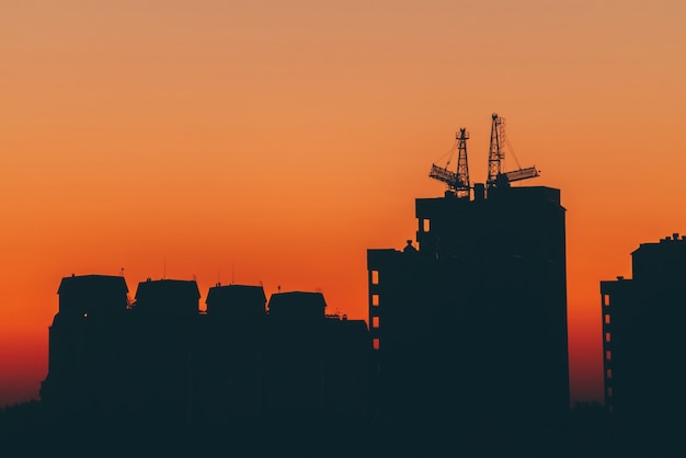 Cityscape with vivid fiery dawn. Amazing warm dramatic cloudy sky above dark silhouettes of city buildings.