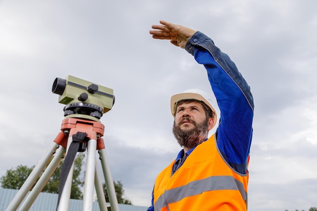 Foto un ingegnere civile con un livello ottico agita la mano per controllare i colleghi da lontano