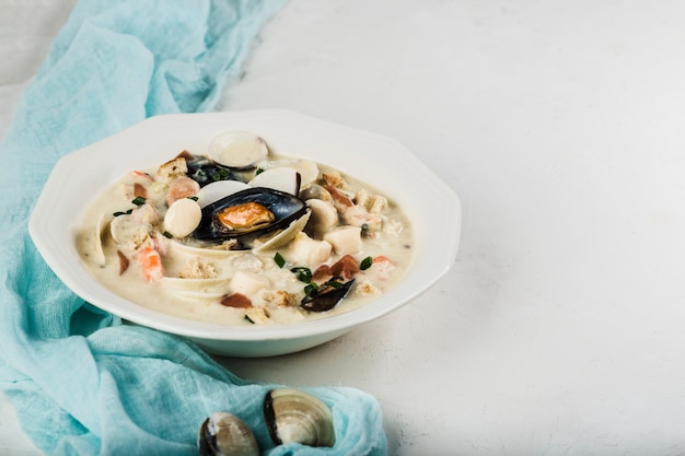 Clam chowder in a white plate. The main ingredients are shellfish, broth, butter, potatoes and onions.