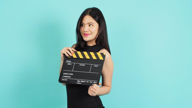 Clapper board or movie clapperboard in teenage girl or woman hand with black and yellow color.it use in video production ,film, cinema industry on green or Tiffany Blue background.she wear black dress