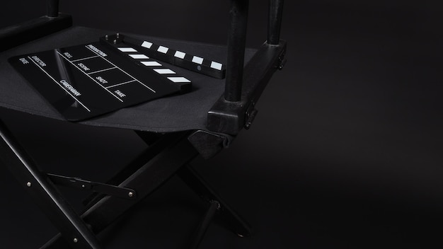 黒の背景で映画製作に使用されるディレクターズチェア付きのカチンコまたは映画スレート