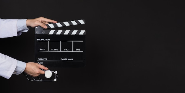 Clapper board and stethoscope in doctor's hand on black background