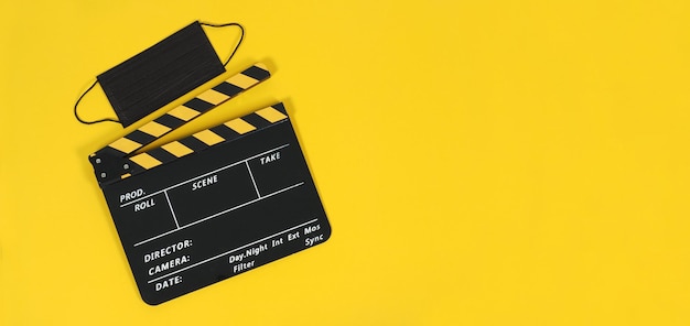 Clapper board in yellow and black color and black face mask on yellow background.