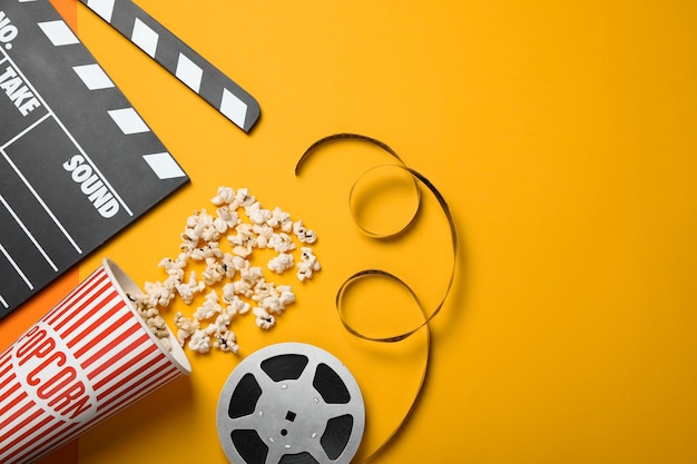 Clapperboard popcorn and film reel on orange background flat lay Space for text