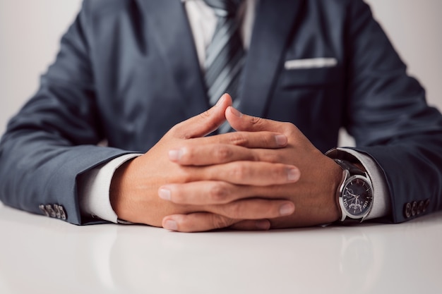 Clasped hands of a businessman in a formal suit sitting at a work or meeting table