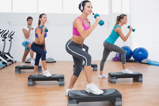 Class performing step aerobics exercise with dumbbells