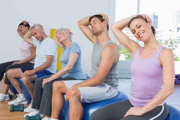 Class sitting on exercise balls and stretching neck in gym