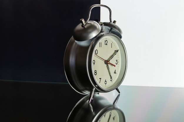 Photo classic alarm clock on a black and white background with reflection on the surface. concept for advertising and design. close-up.