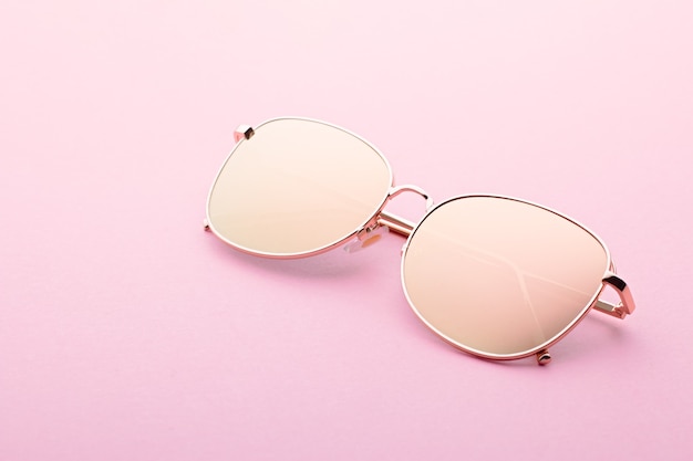 Classic aviator mirrored flat lens sunglasses with golden metal frame closeup on pink background, top view