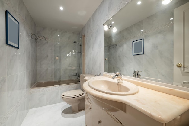 Классическая ванная комната с кремовыми шкафчиками, столешницей в тон, большим зеркалом на стене и кремовой ванной с экраном
