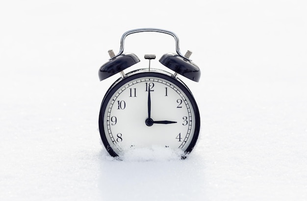 雪の中のクラシックな黒い目覚まし時計 冬の到来のコンセプト 時計は 15 時を示しています