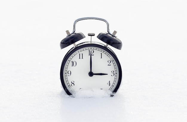 Classic black alarm clock in the snow The concept of the arrival of winter The clock shows 15 o'clock