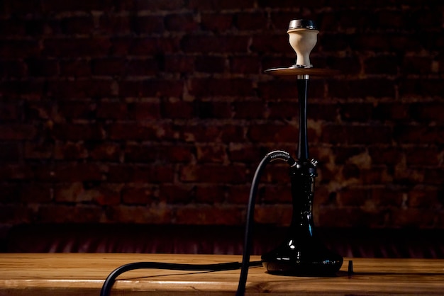 classic black hookah stands alone on a wooden table with a brick wall in the background . high quality photo