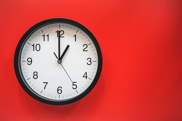 Classic black and white analog clock on red background at One o'clock with copy space