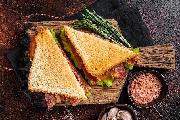 Classic BLT sandwich with bacon tomato and lettuce on wooden board with herbs Dark background Top view