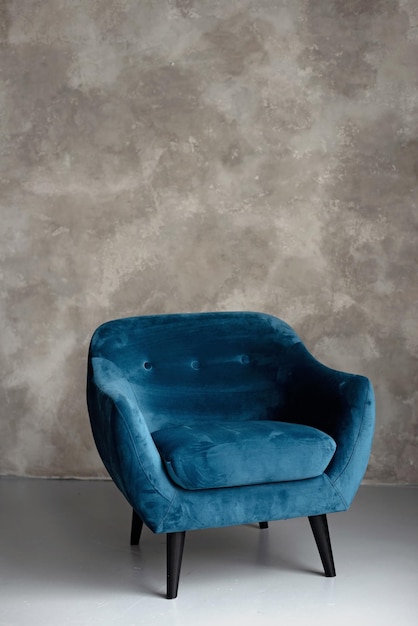 Classic blue velvet art deco armchair with wooden legs against a gray wall Front view Soft selective focus