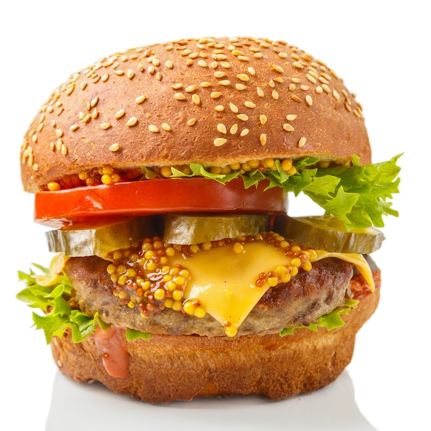 Classic burger with beef, cheese vegetables in sauce on a bun with sesame seeds on a wooden round stand on a white plate