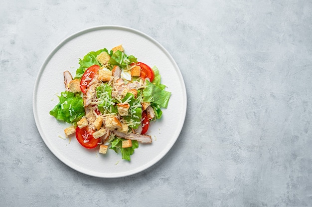 Classic Caesar salad with chicken breast on a gray background. Top view with copy space. Healthy food.