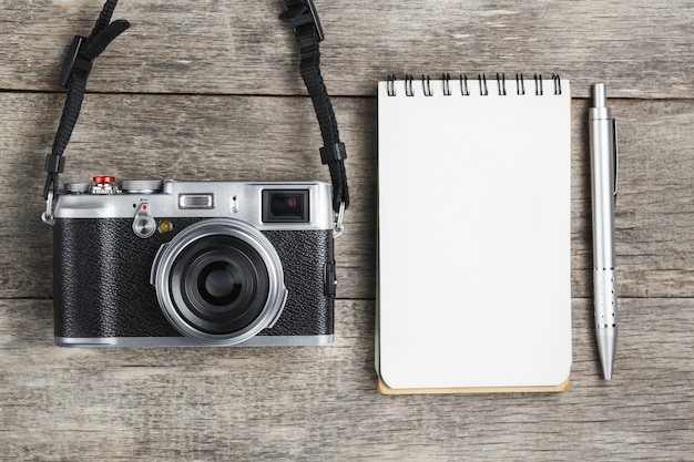 Классическая камера с пустой страницей блокнота и серой ручкой на сером деревянном, винтажном столе