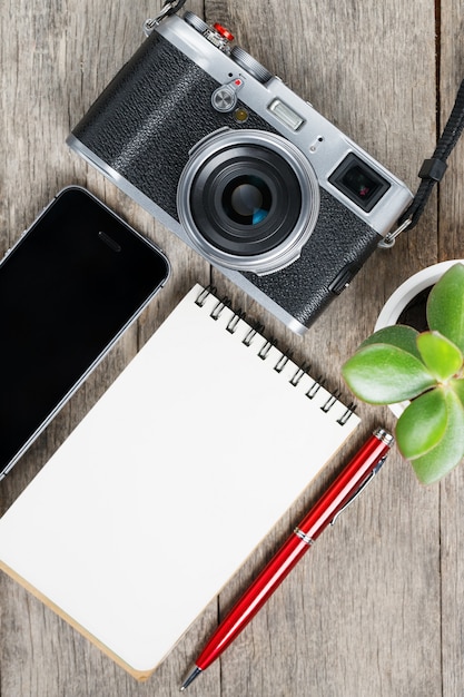 Classic camera with blank notepad page and red pen on gray wooden, vintage desk with telephone.