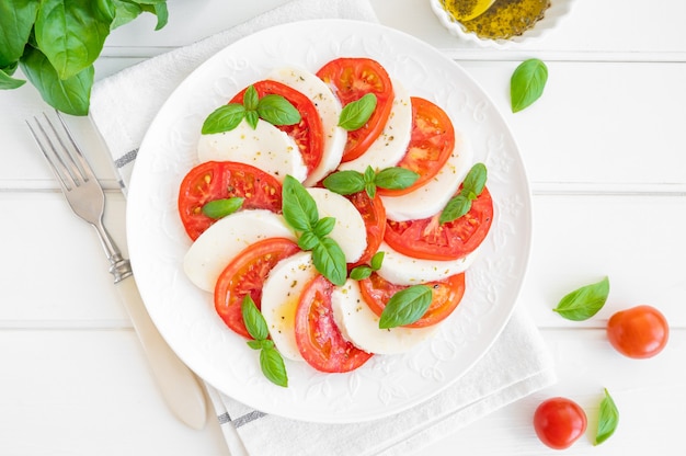 Classic caprese salad with mozzarella cheese tomatoes and basil on a white plate