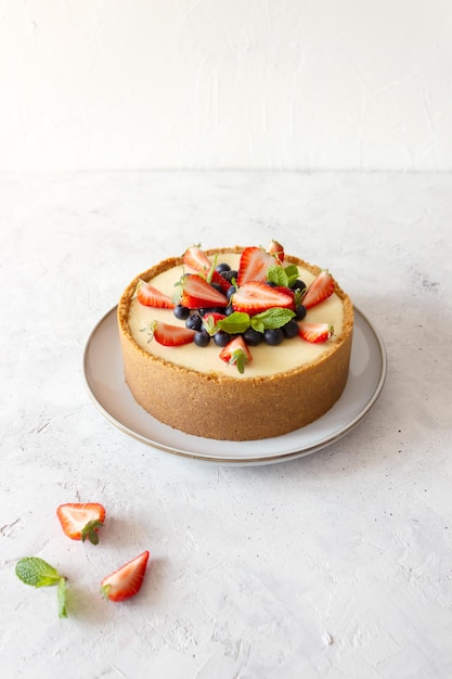 회색 접시 흰색 배경에 딸기 블루베리 민트로 장식된 클래식 치즈 케이크