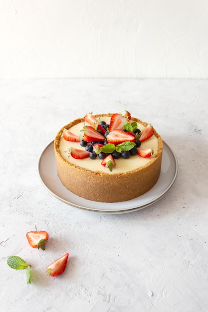 Foto classica cheesecake decorata con fragole mirtilli menta su fondo bianco piatto grigio