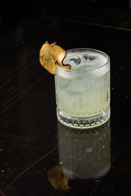 Classic cocktail glass on glass table in night club restaurant\
alcohol cocktail drink garnish with apple chips closeup modern\
alcoholic beverage