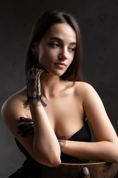 Photo classic dark studio portrait of a young brunette woman in black clothes who is sitting on a chair