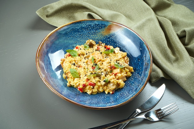 The classic dish of Italian cuisine - risotto with seafood, vegetables and spices in a blue bowl on a wooden table