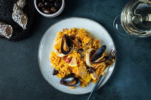 Classic dish of Spain, seafood paella in plate on blue background top view. Spanish paella with shrimps, clamps, mussels and fresh lemon. Spanish food. Comfort food. Rice with seafood.