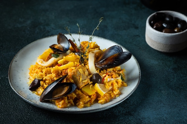 Classic dish of Spain, seafood paella in plate on blue background top view. Spanish paella with shrimps, clamps, mussels and fresh lemon. Spanish food. Comfort food. Rice with seafood.