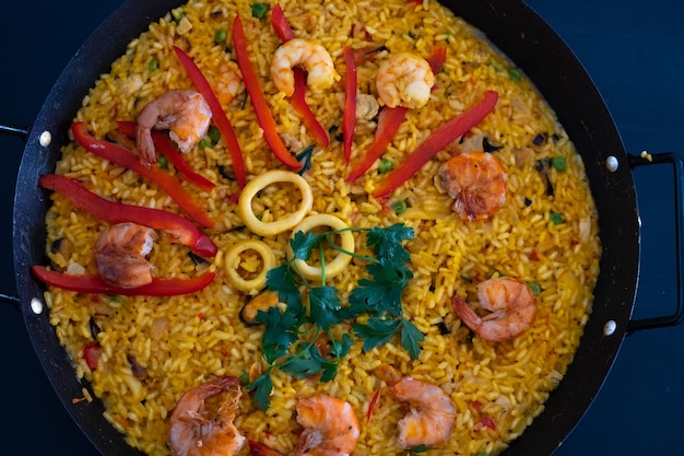 Classic dish of Spain seafood paella in traditional pan on dark blue background top view