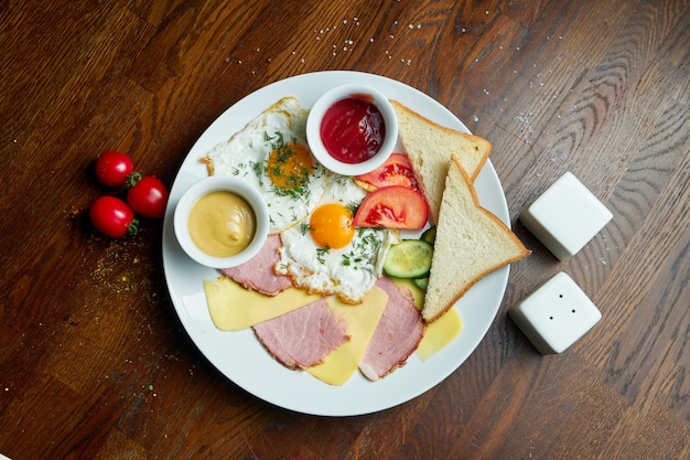 Classic English breakfast: toasts, smoked sausages, fried eggs, potato and fried toasts on a white plate