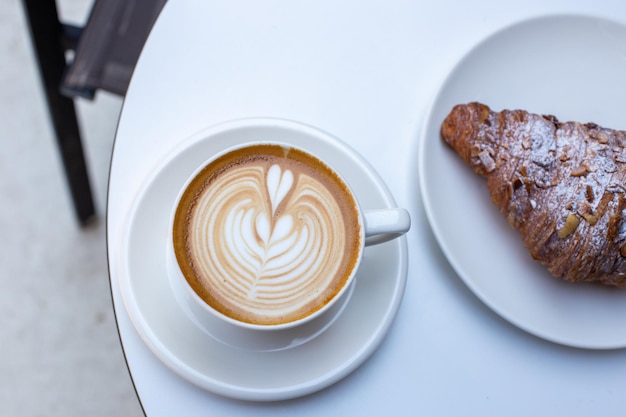 Classico croissant francese alle mandorle e tazza bianca al caffè con cappuccino