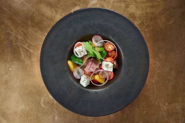 Classic greek salad with feta cheese in plate on metal background.