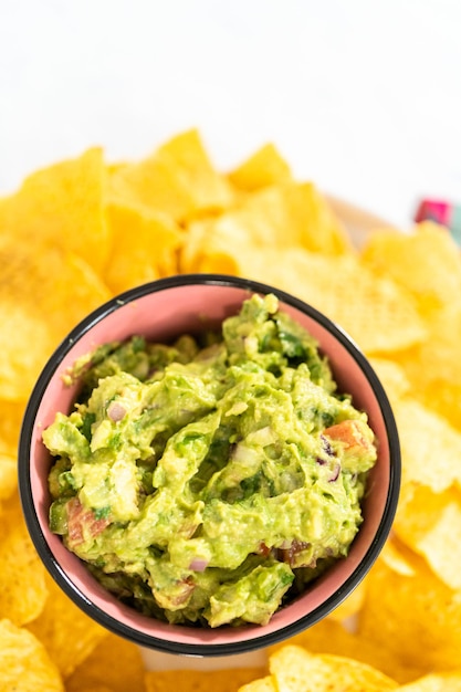 Classic guacamole dip in a small bowl with corn tortilla\
chips.