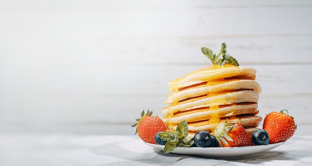 On classic homemade pancakes with berries on a white saucer on a light wooden background in a rustic style