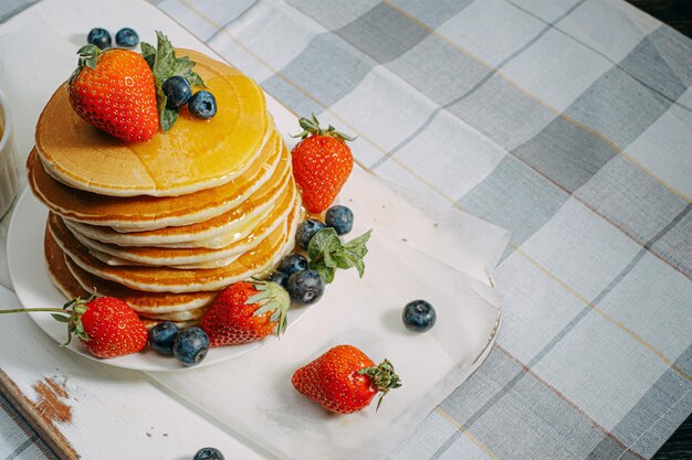 On classic homemade pancakes with berries on a white saucer on a light wooden background in a rustic style