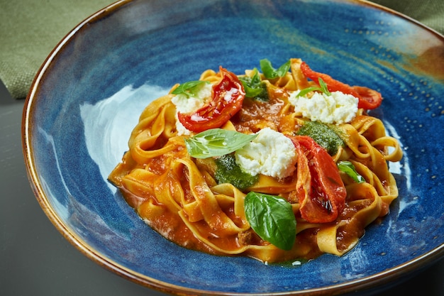 Classic, homemade pasta bolognese with tomatoes, basil and cream cheese in a blue bowl on a wooden table. Selective focus. Close up